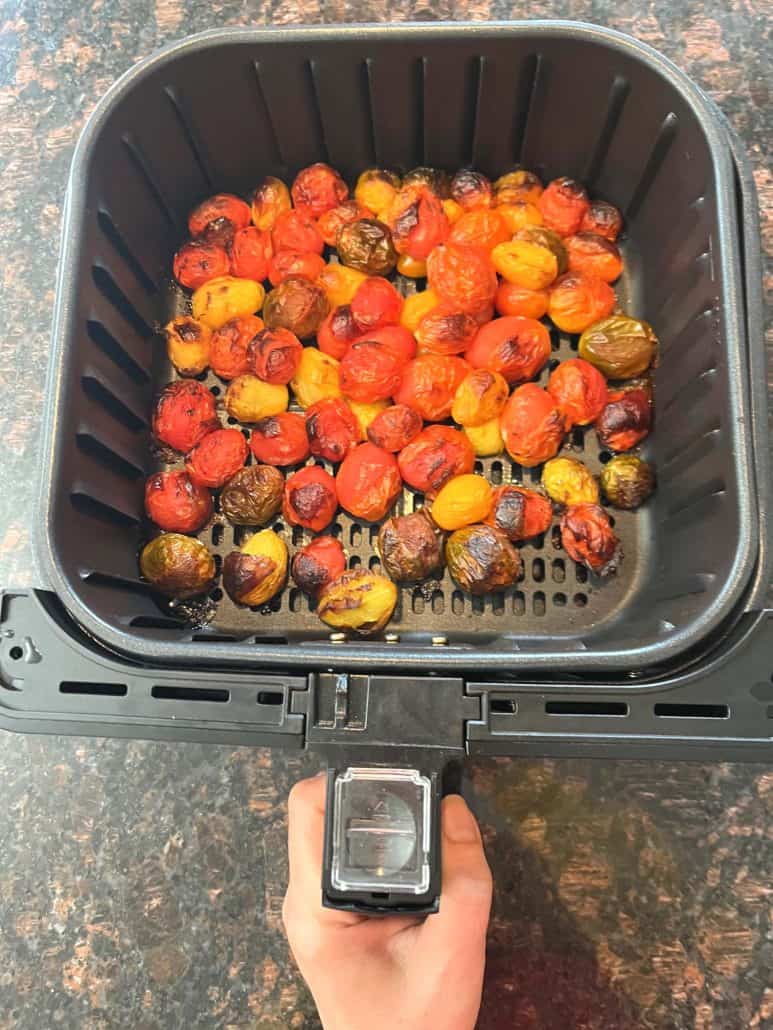 Freshly roasted medley tomatoes in an air fryer basket, perfectly blistered and ready to season.