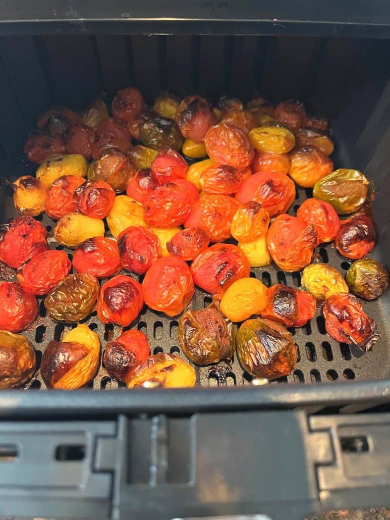 Roasted medley tomatoes in the air fryer basket, showing caramelized skins and vibrant colors.