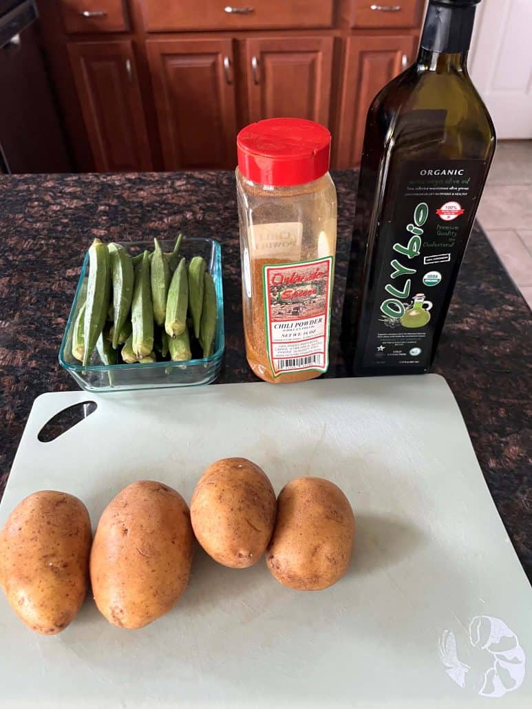 Fresh ingredients for air fryer okra and potatoes laid out on a counter, including potatoes, okra, chili powder, and olive oil, ready for prep.