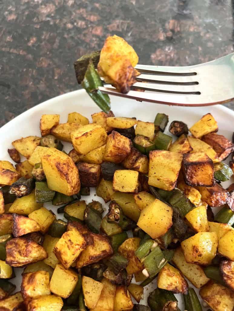 Fork holding a bite of crispy air fryer okra and potatoes above a plate, ready to enjoy this flavorful and healthy dish.