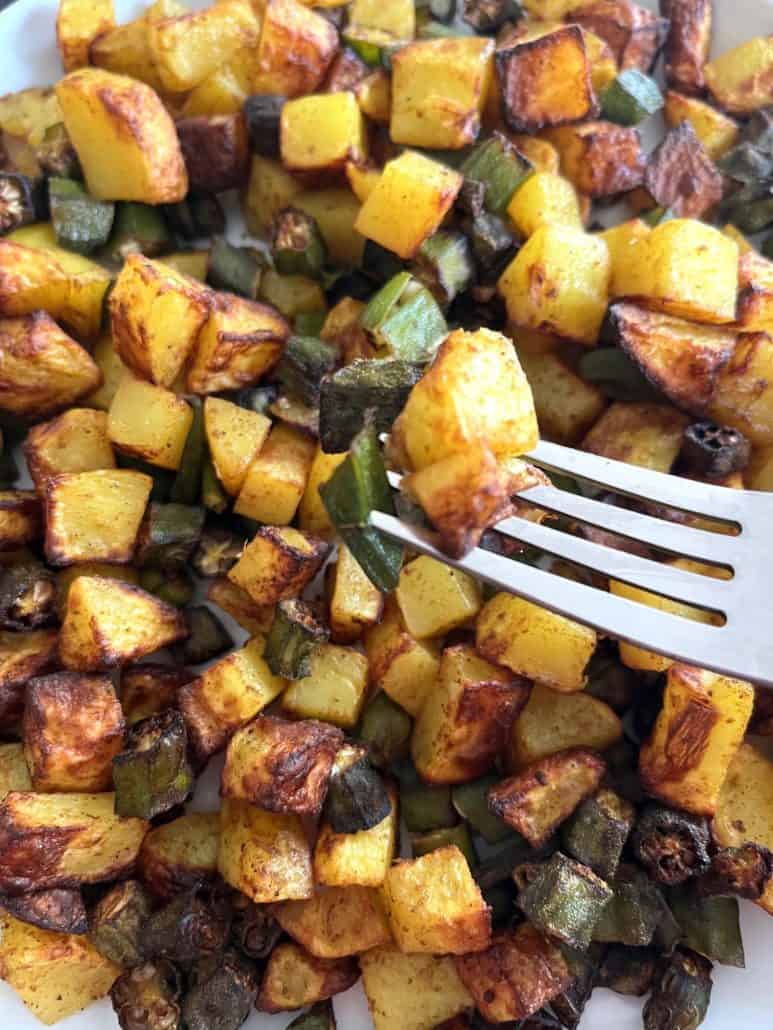 Close-up of air fryer okra and potatoes with a fork picking up a golden, crispy bite from a flavorful and perfectly roasted batch.