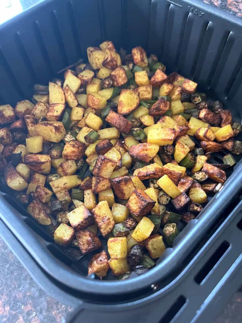 Angled view of cooked okra and potato cubes in the air fryer basket, showing their crispy texture and golden brown color after roasting.