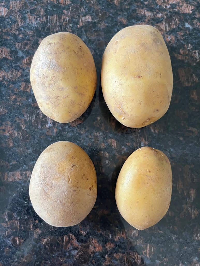 Four washed organic potatoes with skin on, ready to be cubed and seasoned for the Air Fryer Skin On Potatoes recipe.