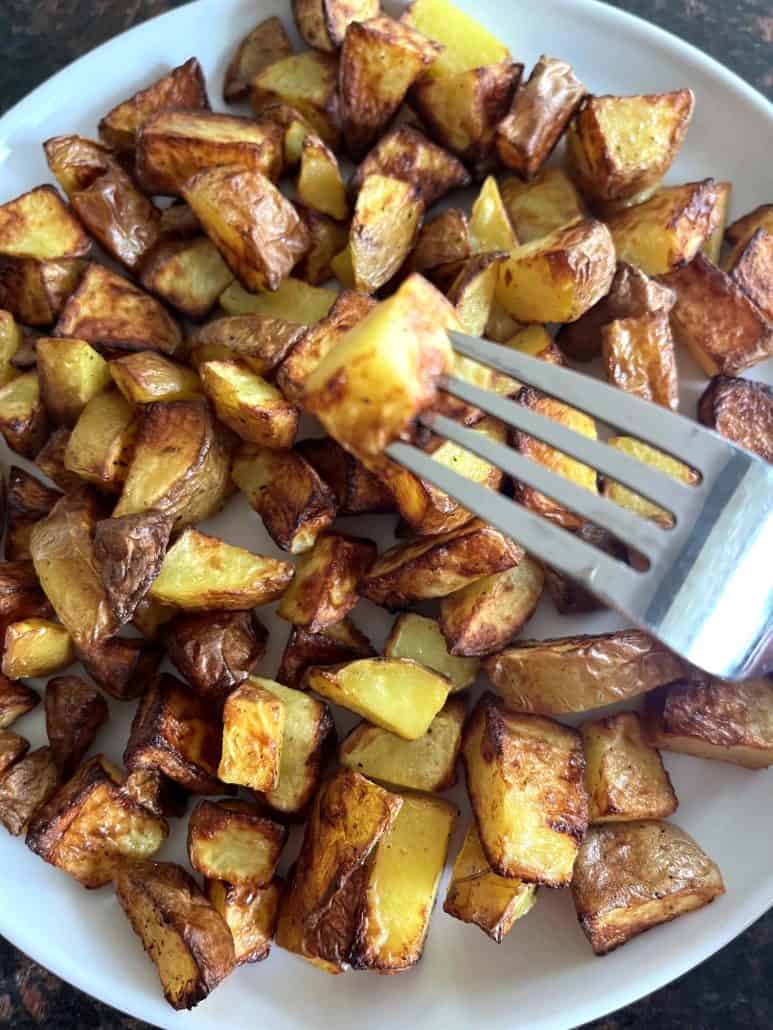 Fork picking up a crispy, golden skin-on potato cube from a plate.