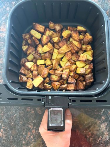 Golden brown skin-on potato cubes freshly cooked in the air fryer basket, perfectly crisped and ready to serve.