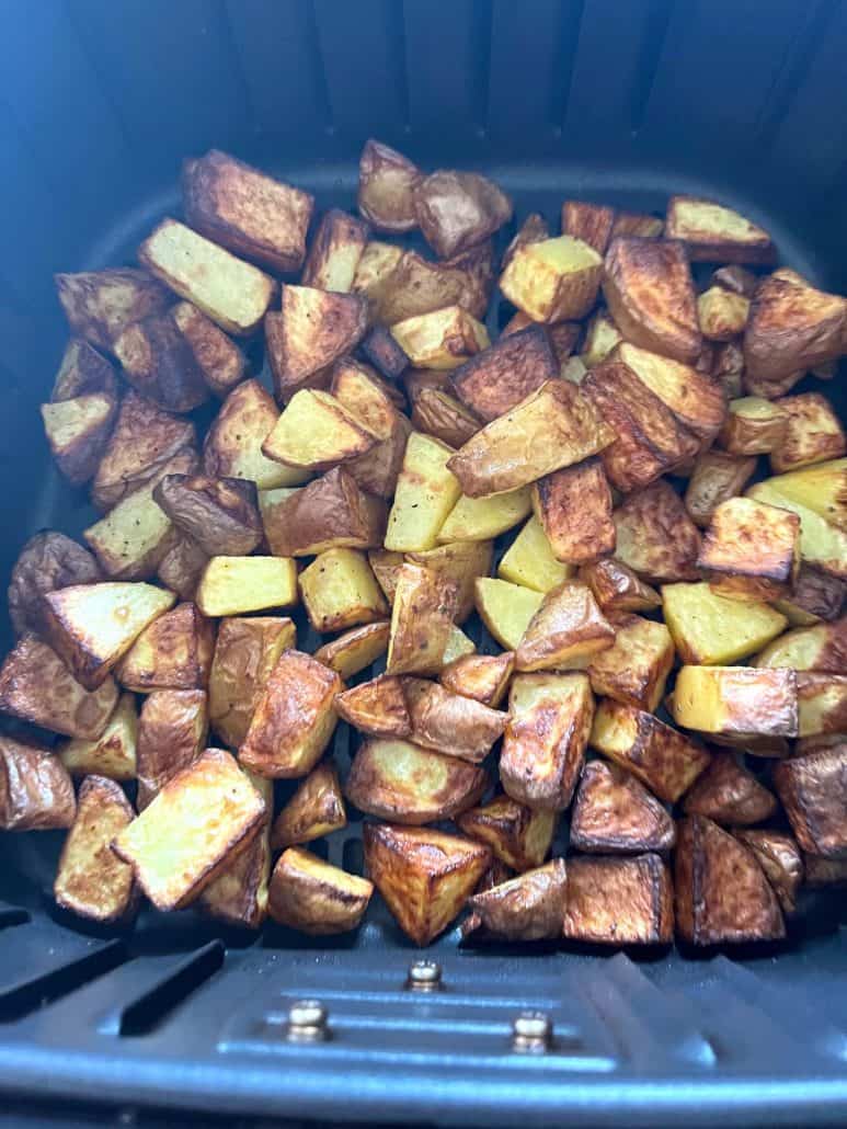 Freshly air fried skin-on potato cubes in the basket, golden brown and evenly roasted.