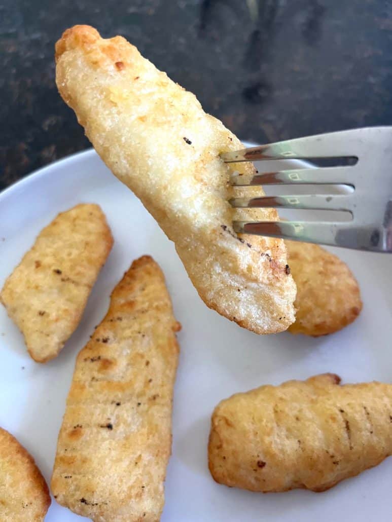Fork holding a crispy piece of Trader Joe’s battered halibut with more fillets on a plate below, showing the golden crust from air frying.