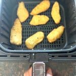 Frozen breaded halibut fillets cooking in an air fryer basket, shown as part of the Air Fryer Trader Joe’s Battered Halibut recipe.