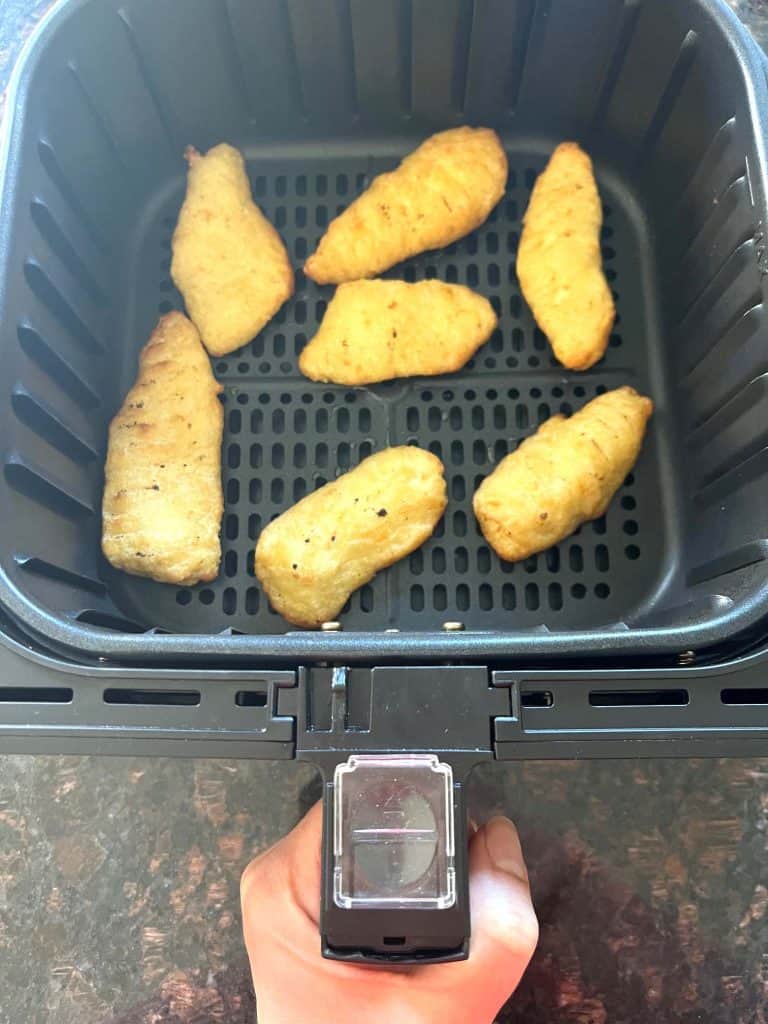 Frozen breaded halibut fillets cooking in an air fryer basket, shown as part of the Air Fryer Trader Joe’s Battered Halibut recipe.