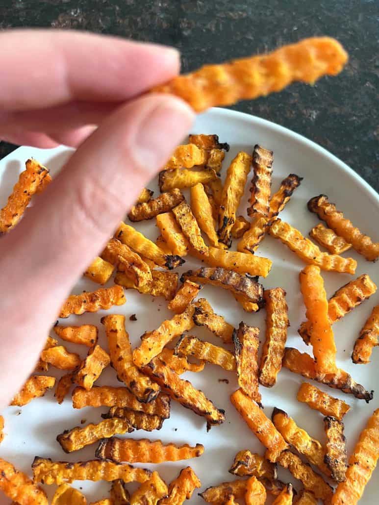 Hand holding a crispy air-fried Trader Joe’s Butternut Squash Zig-Zag above a plate, showing the perfect golden texture.
