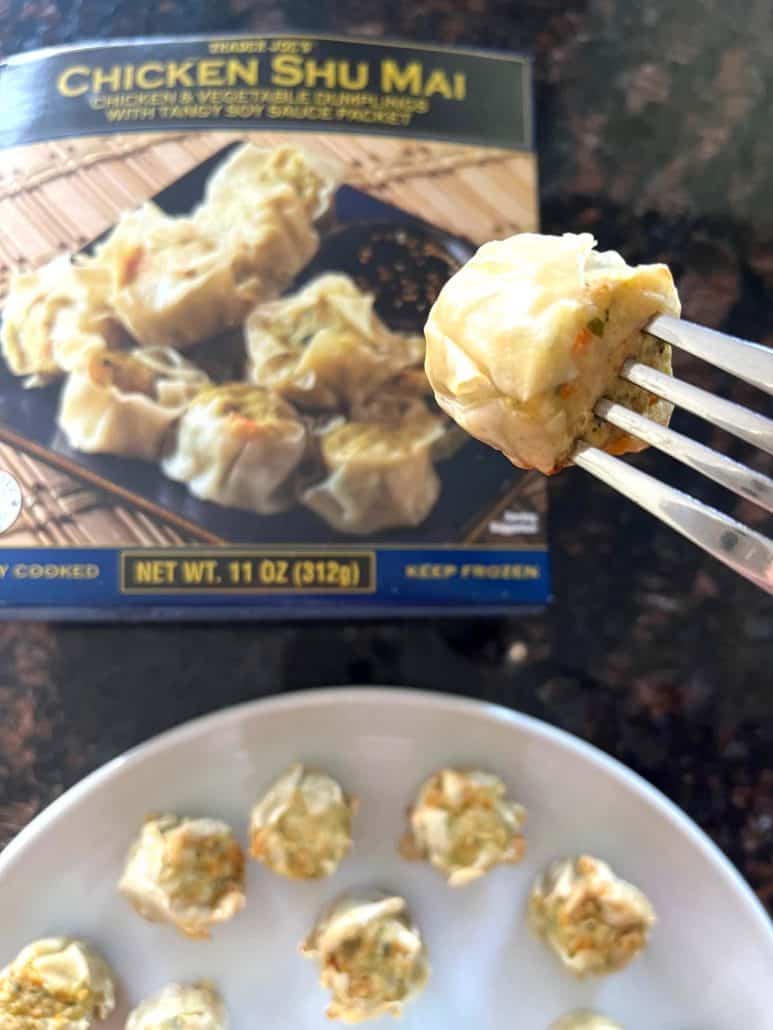 Cooked Trader Joe’s Chicken Shu Mai served on a plate with one dumpling held up on a fork in front of the product box.