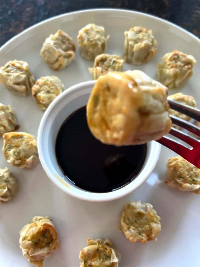 Fork holding a cooked Trader Joe’s Chicken Shu Mai dumpling above a dipping sauce cup.