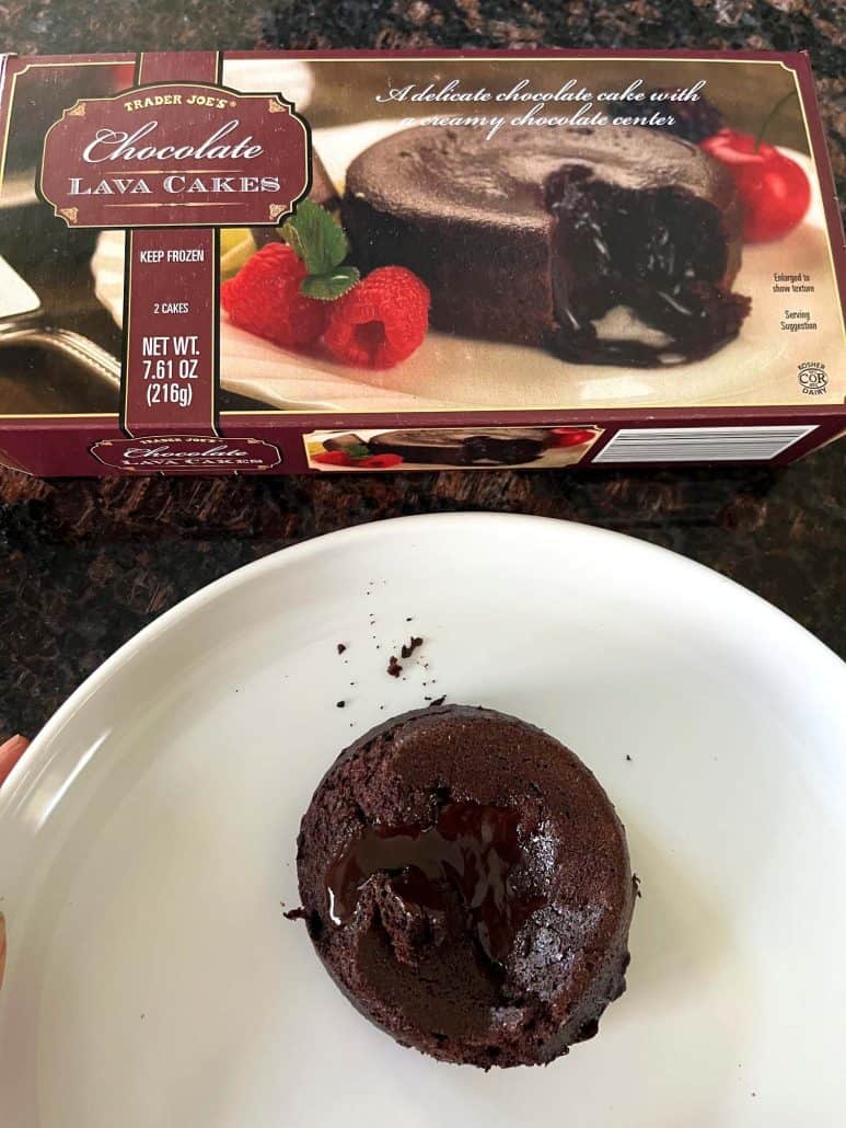 Cooked Trader Joe’s chocolate lava cake served on a white plate with the product box in the background, showing the rich, gooey center ready to enjoy.