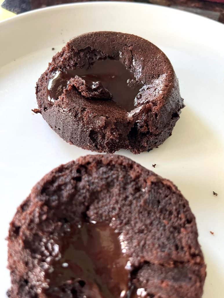 Two Trader Joe’s chocolate lava cakes on a plate, cut open to reveal the gooey, melted chocolate center inside.