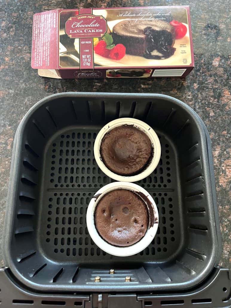 Two baked Trader Joe’s chocolate lava cakes in the air fryer basket with the product box in the background.