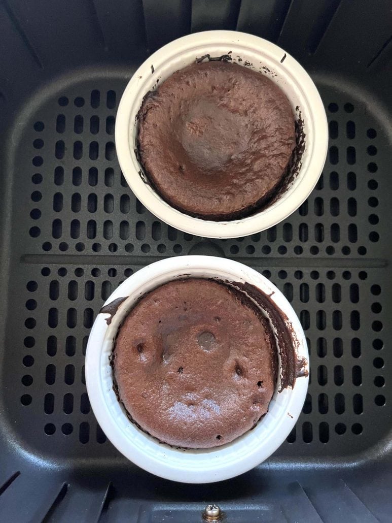 Two fully cooked Trader Joe’s chocolate lava cakes in their oven-safe cups inside the air fryer basket, showing the finished texture before serving.