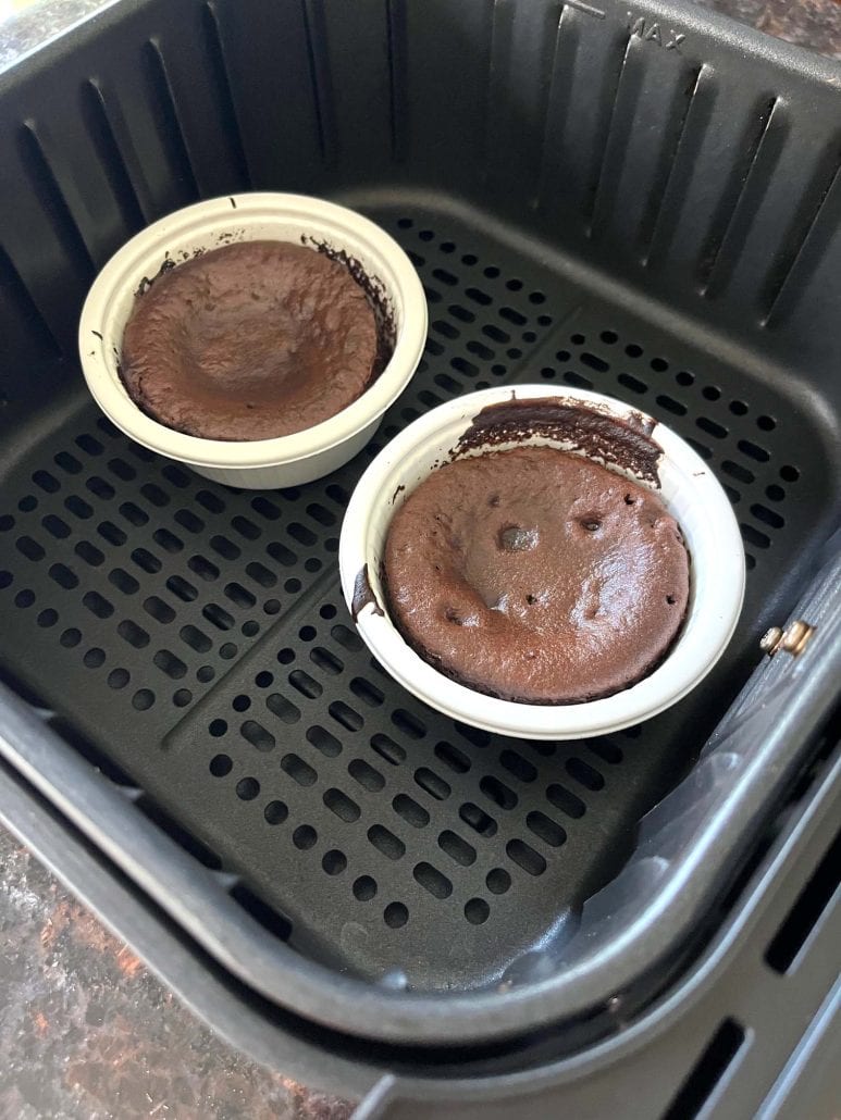Angled view of two cooked Trader Joe’s chocolate lava cakes inside the air fryer basket, ready to be removed and served warm.