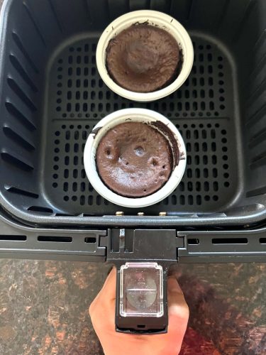 Two Trader Joe’s chocolate lava cakes cooking in an air fryer basket, showing how they are baked directly in their oven-safe cups from frozen.