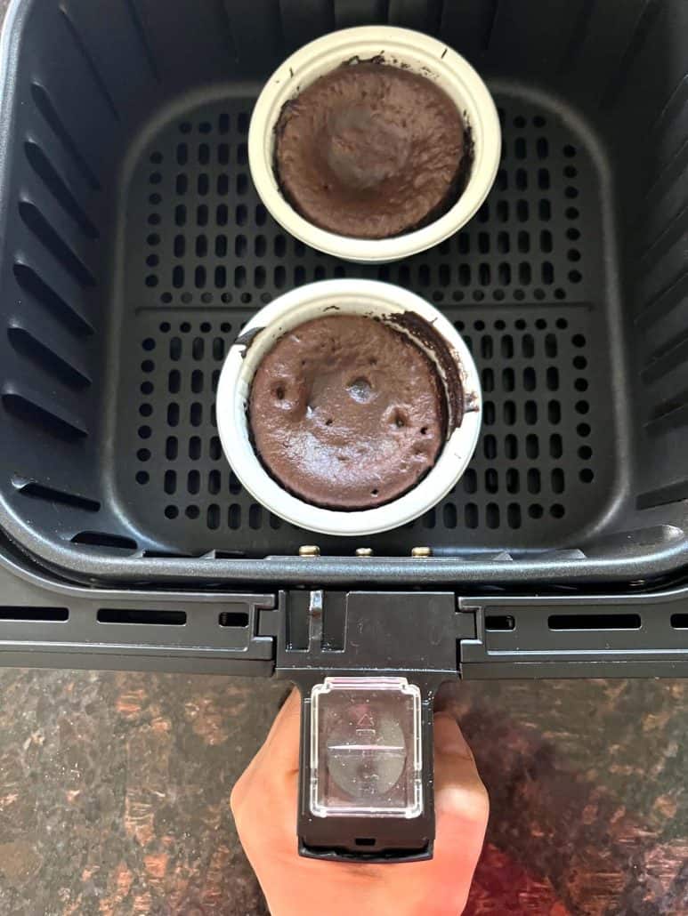 Two Trader Joe’s chocolate lava cakes cooking in an air fryer basket, showing how they are baked directly in their oven-safe cups from frozen.
