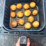 Melanie Mendelson from melaniecooks.com holding the air fryer basket with golden brown dough balls inside, perfectly crisped and ready to be enjoyed.