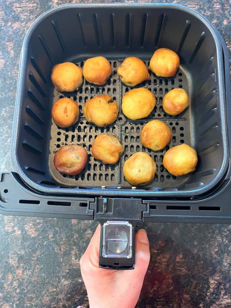 Melanie Mendelson from melaniecooks.com holding the air fryer basket with golden brown dough balls inside, perfectly crisped and ready to be enjoyed.