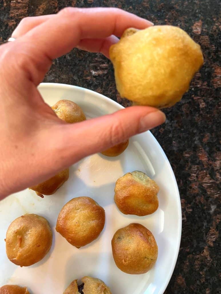 Melanie Mendelson from melaniecooks.com holding a golden brown air-fried dough ball above a plate of similar dough balls, showcasing its crispy texture.