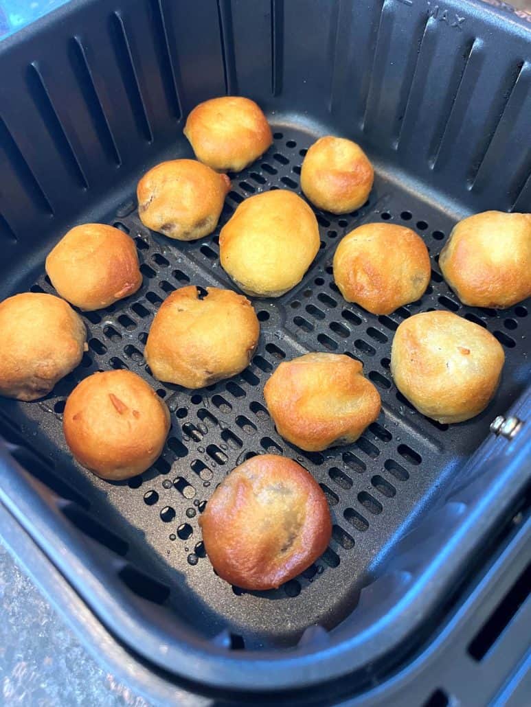 Golden brown air-fried dough balls in a basket, some with a perfectly crispy exterior and a few with slight darker spots.
