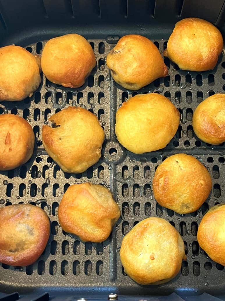 Air fryer basket filled with golden brown dough balls, showing a perfect crispy texture with some light variations in color.