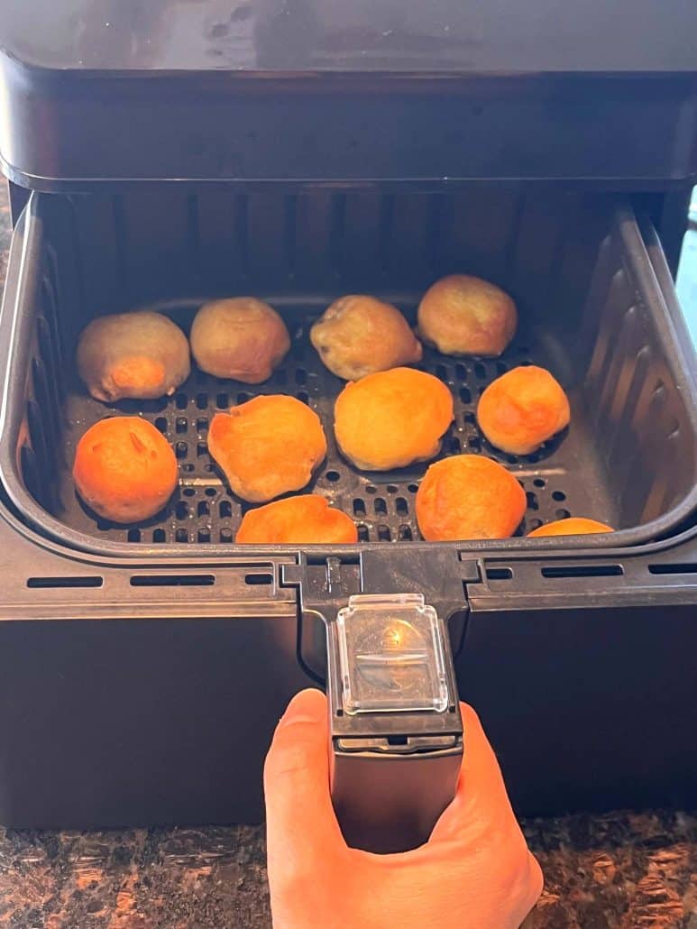 Melanie Mendelson from melaniecooks.com holding the air fryer basket, showing golden brown dough balls inside.