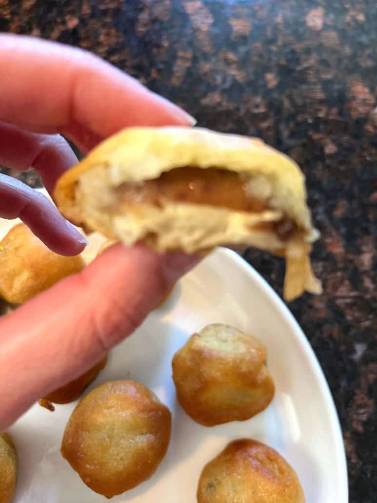 Melanie Mendelson from melaniecooks.com holding a golden brown air-fried dough ball with a bite taken out, revealing the soft, fluffy interior.