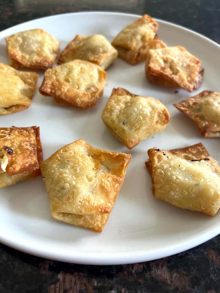 Side view of crispy jalapeño cream cheese wontons on a white plate, freshly air fried.