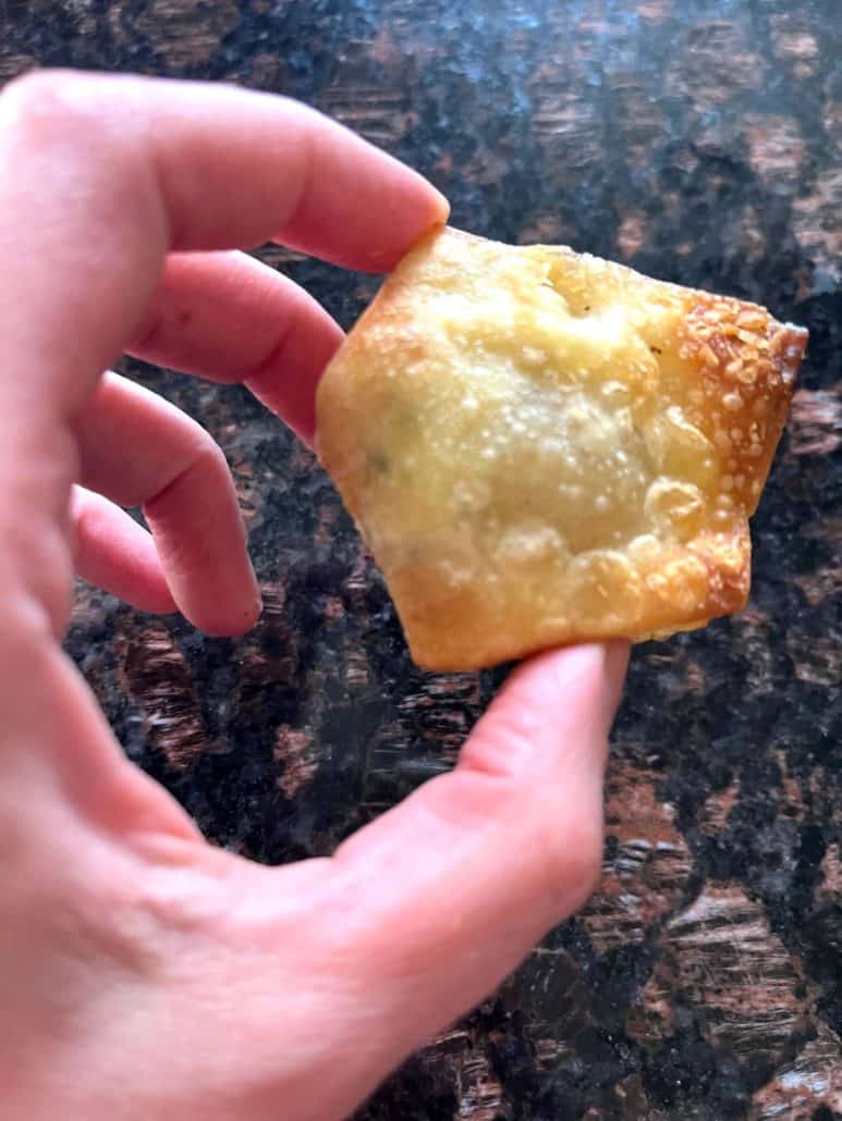 Close-up of a hand holding a crispy air-fried Trader Joe’s wonton, showing its golden brown texture.