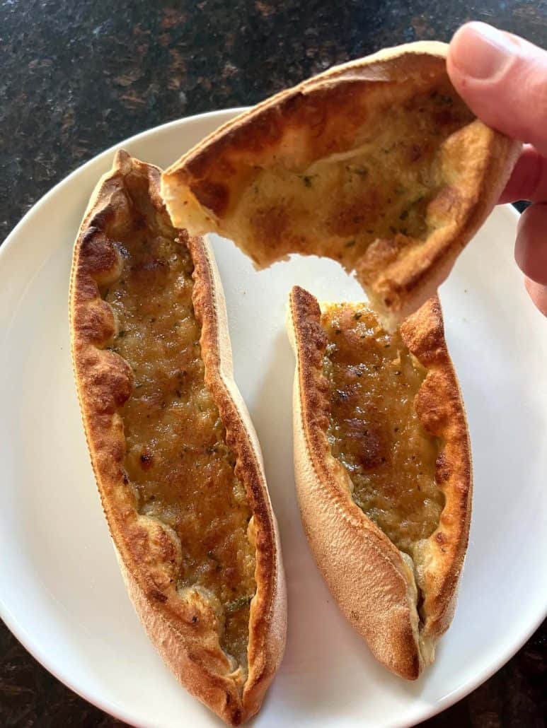 Two cooked Trader Joe’s Garlic Gondolas on a white plate, with one piece being pulled apart to reveal the melted cheesy filling inside.