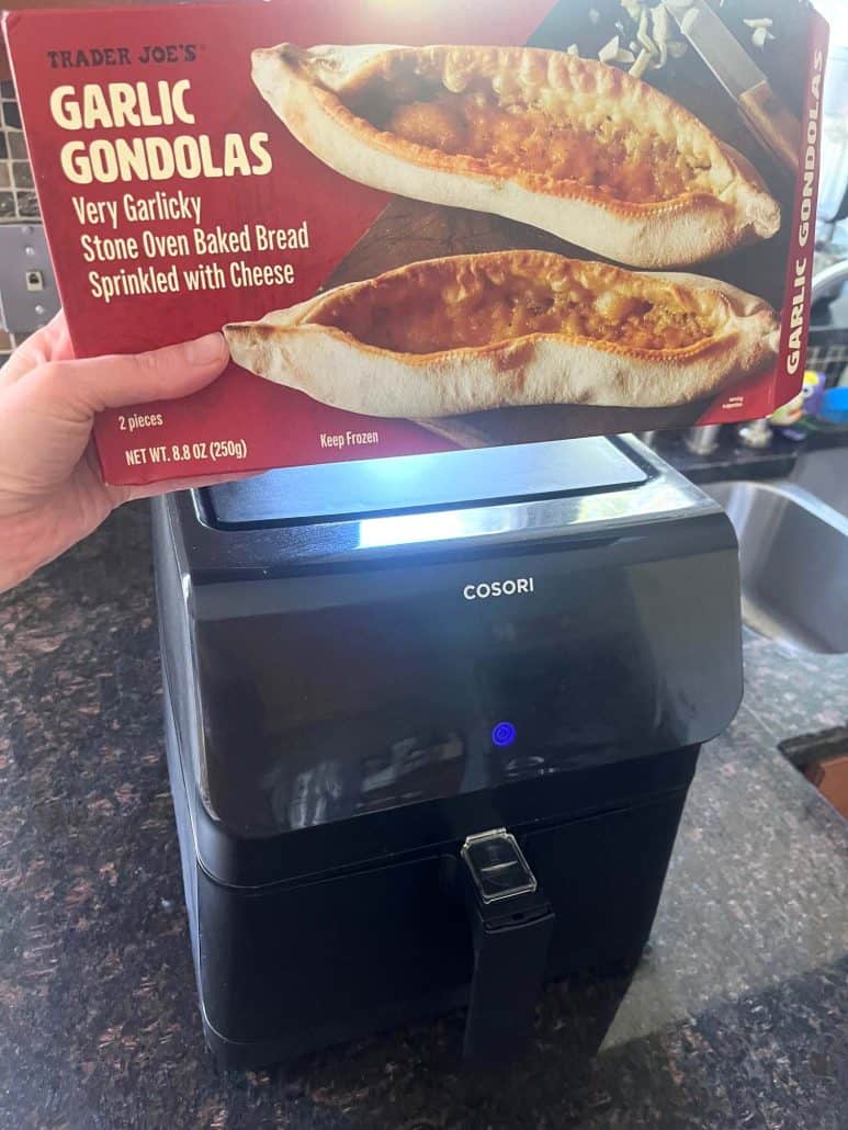 Holding a box of Trader Joe’s Garlic Gondolas in front of an air fryer, ready to start cooking for the easy Air Fryer Garlic Gondolas recipe.