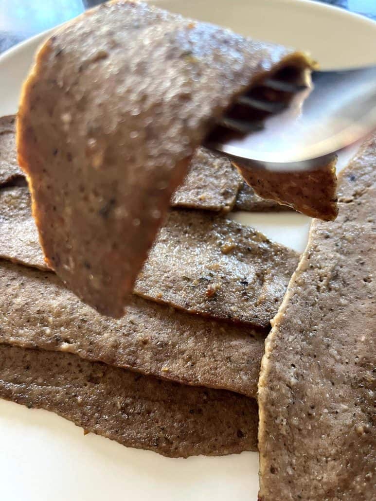 Fork lifting a tender, browned slice of Trader Joe’s gyro meat above a plate filled with air-fried slices.