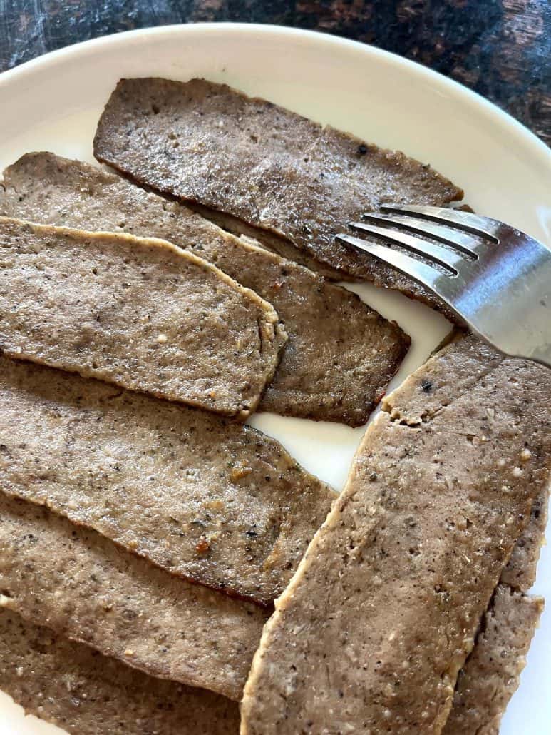 Fork lifting a slice of air-fried Trader Joe’s gyro meat from a white plate with several cooked slices.