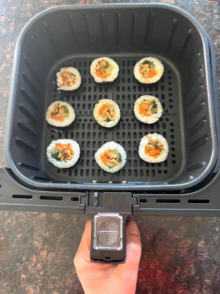 Frozen Trader Joe's kimbap arranged in a single layer inside an air fryer basket before cooking.