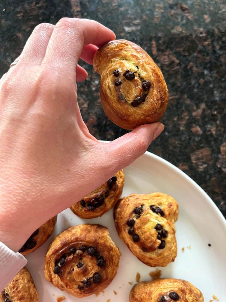 Hand picking up a golden, chocolate-filled Trader Joe’s Mini Croissant from a plate.