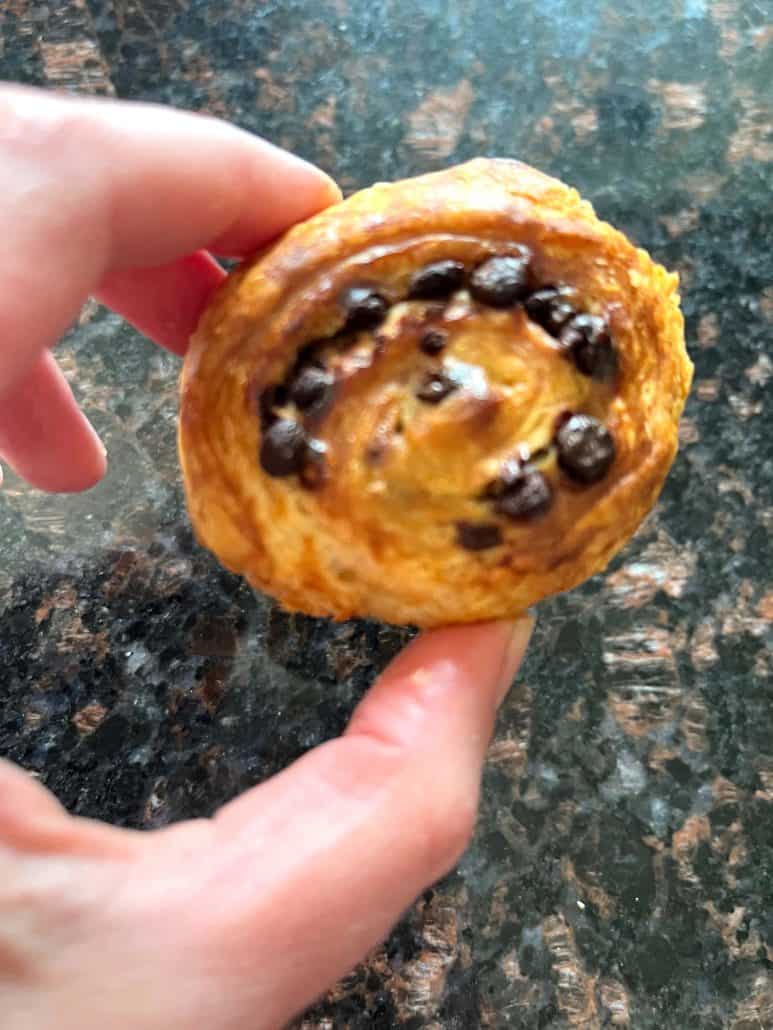 Hand holding a golden-brown Trader Joe’s Mini Croissant with visible chocolate chips, freshly baked and ready to enjoy.