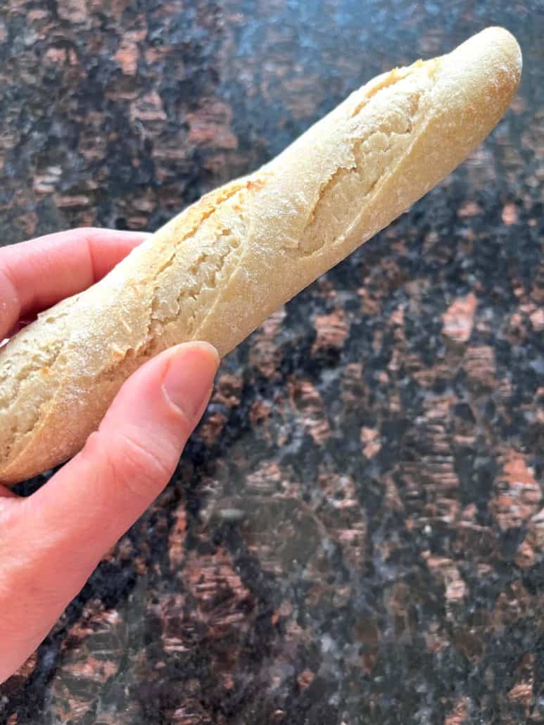 Close-up of a hand holding one frozen Trader Joe’s mini French baguette.