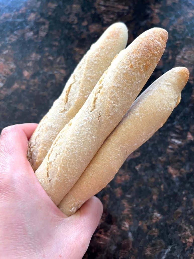Hand holding three frozen Trader Joe’s mini French baguettes, ready to be cooked in the air fryer.