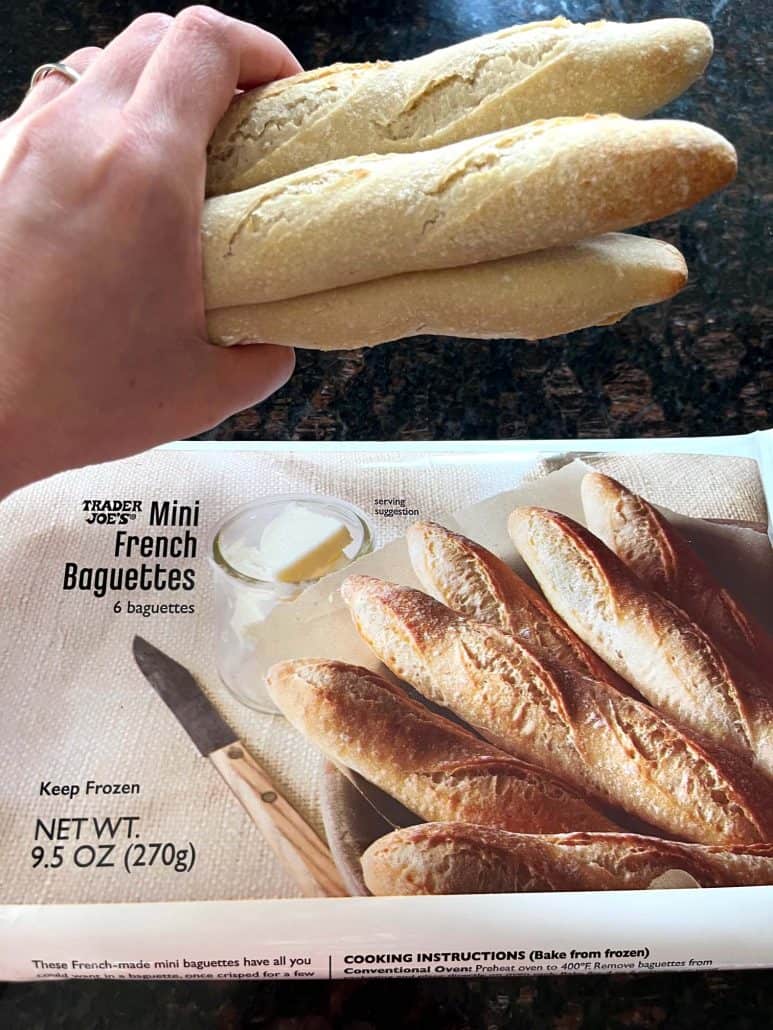 Hand holding frozen Trader Joe’s mini French baguettes above the product packaging.