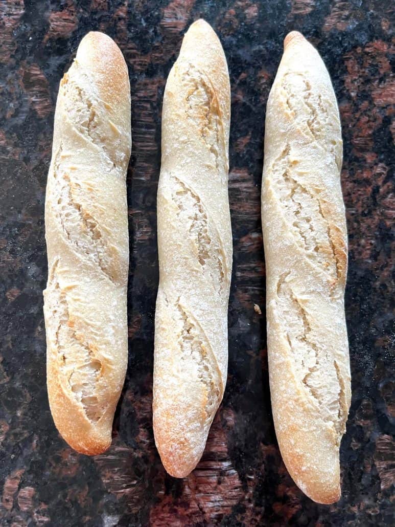 Three cooked Trader Joe’s mini French baguettes placed on a countertop, fresh from the air fryer and ready to serve as shown in the easy bread recipe.