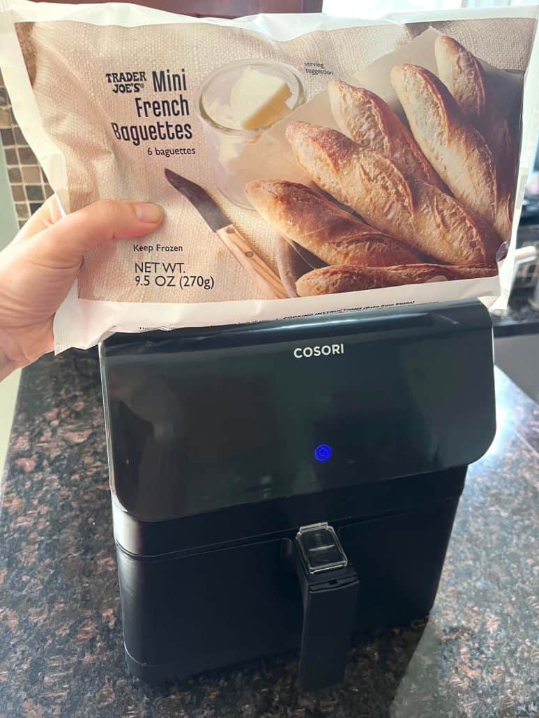 Holding a bag of Trader Joe’s mini French baguettes in front of an air fryer, ready to cook.