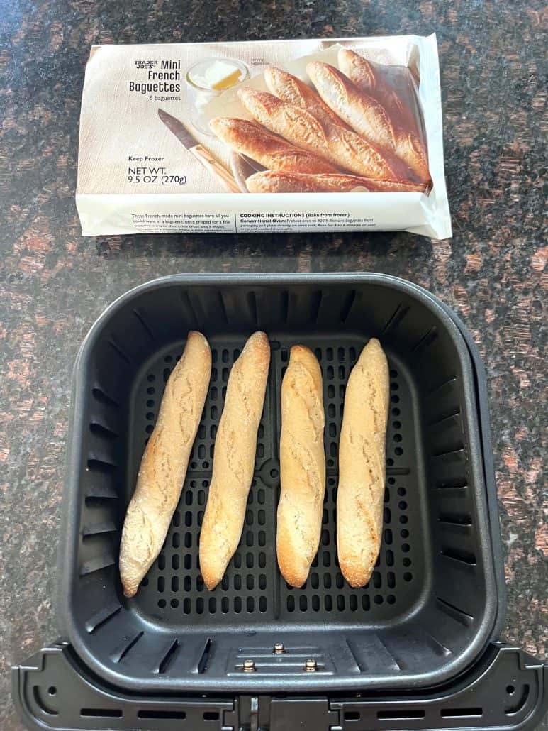 Air fryer basket with cooked Trader Joe’s mini French baguettes placed below the original packaging, showing the before and after.