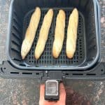 Frozen Trader Joe’s mini French baguettes arranged in a single layer inside an air fryer basket, ready to cook.