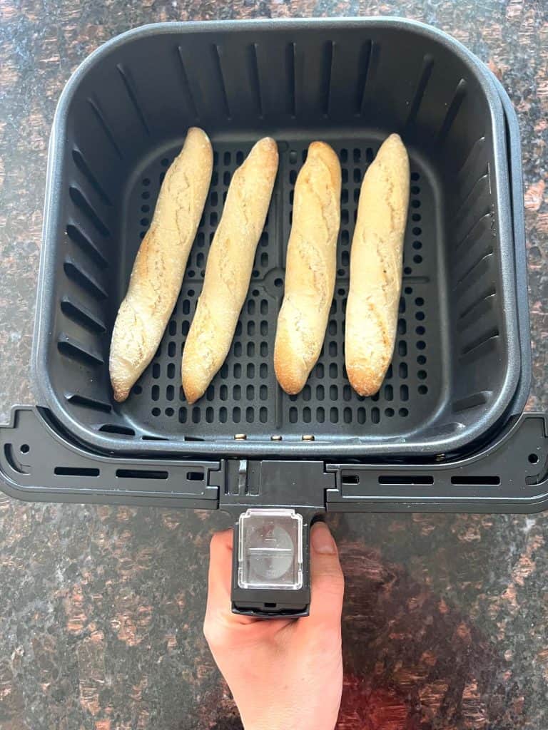 Frozen Trader Joe’s mini French baguettes arranged in a single layer inside an air fryer basket, ready to cook.