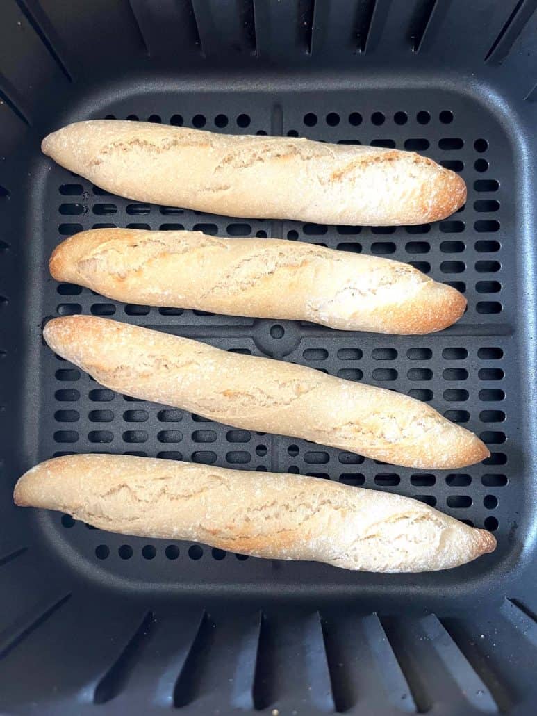 Four fully cooked Trader Joe’s mini French baguettes in the air fryer basket, perfectly crisped.