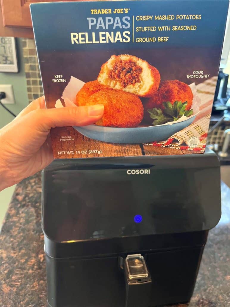 Holding a box of Trader Joe’s Papas Rellenas in front of an air fryer before cooking.