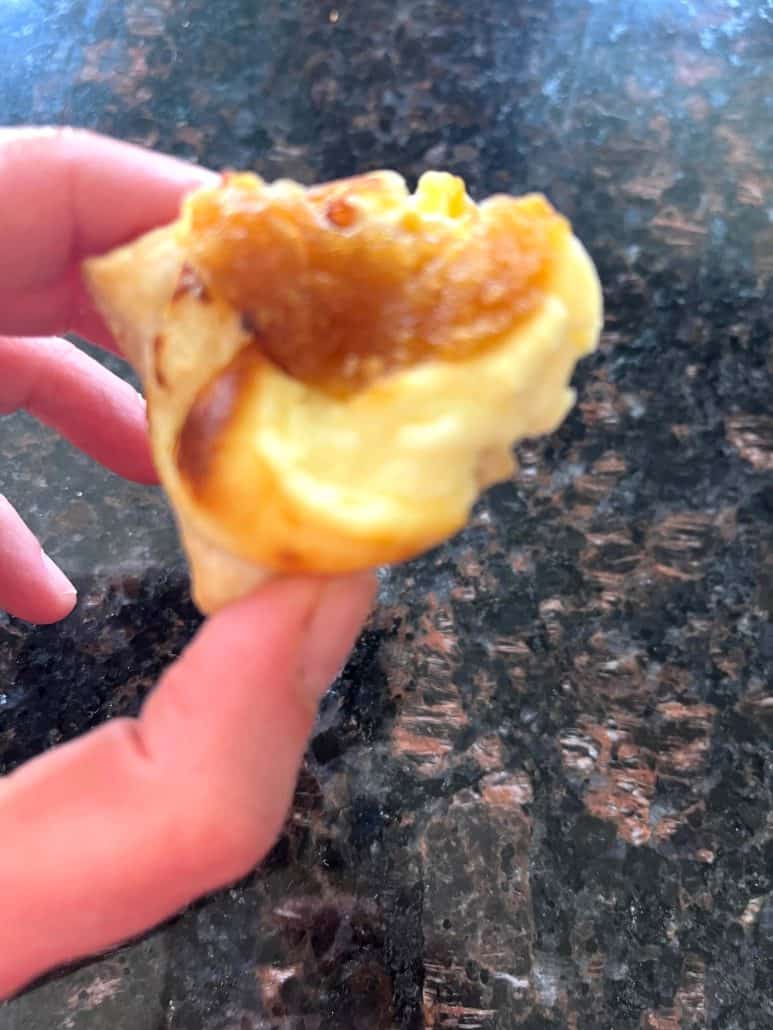 Hand holding a warm Trader Joe’s Pastry Bite with gooey melted cheese and caramelized onion filling after air frying.